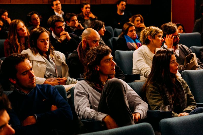An audience in theatre seats listens closely to a talk.