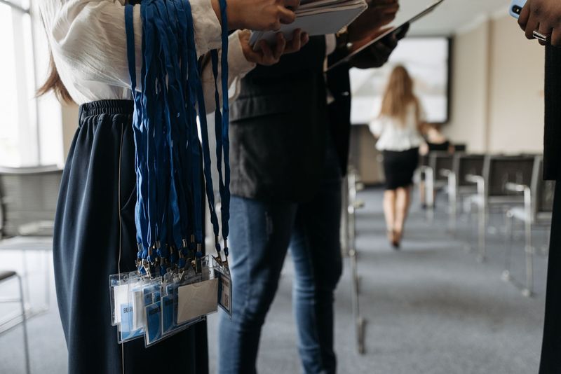 A person holds a bundle of blue lanyards with attendee badges in a conference room.