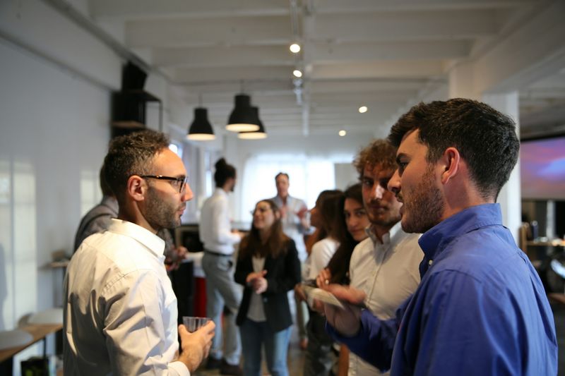 Two men deep in conversation at a daytime meetup, with other guests talking behind them.